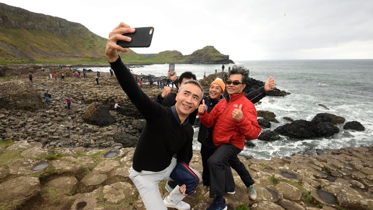 Visitors taking a selfie with a mobile phone at Giant's Causeway, County Antrim with the sea behind
